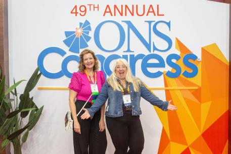 Two female congress attendees standing in front of Congress 2024 poster background, smiling excitedly at the camera